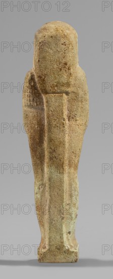 Ushabti, Wigs, beards facial hair, funerary figurine mummy-shaped, hoes, grave goods. Standing on a base, supported at the back by a pillar/pilaster. Arms crossed on the chest, only the hands protrude from under the shroud, placed at the same level slightly apart. Hoes in both hands; the ends of the hoes' handles are slightly curled. In the right hand an additional twisted rope, on which a basket is slung over the left shoulder. Slightly convex tools. On the head a three-part, smooth wig. A long, straight beard tapering toward the bottom, braided into a plait. Large ears, almond-shaped eyes, pronounced eyebrows, broad nose, full lips in a slight grimace. Not inscribed. 664–332 BC; Late Period 26–30th Dynasty, Egypt. Shabti; height 11.7 cm, width 3.2 cm., A vertical stone or ceramic figurine viewed from the back, with a rounded top and a narrow rectangular base, showing a tapered, elongated body with subtle raised ridges along the center and sides, a pronounced seam down the middle of t...