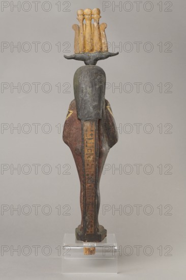 Osiris, Osiris mythology. Figurine in the form of a human mummy wearing a hemhem crown with ram's horns. On the chest is a usekh necklace with falcon heads at the ends. Clenched hands are placed on the chest, one above the other. Below the right hand begins a column of text with the name and filiation. At the back, from the edge of the wig to the feet, a pillar with a column of hieroglyphic inscriptions — the beginning of a hymn to Osiris, the heir of Atum. The figurine is painted cherry red; the visible parts of the body are yellow; the wig is navy blue; the necklace consists of white, red, and blue stripes. The background of the inscriptions is yellow. The figurine belongs to Isetemachbit, a musician of the god Amun-Re, daughter of the priest Mentuemhat; her mother was probably Takereret, known as Heres. Similar to type IV B according to Raven. Dated 4th–3rd century BC; 30th Dynasty–early Ptolemaic period, Egypt. Sculpture; height 54.5 cm, width 12.5 cm, depth 9.5 cm., A carved woode...