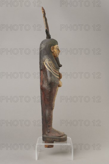 Osiris, Figurine in the form of a human mummy wearing a hemhem crown with ram's horns. On the chest is a usech necklace with falcon heads at the ends. Clenched hands are placed on the chest, one above the other. Below the right hand begins a column of text with the name and filiation. At the back, from the edge of the wig to the feet, a pillar with a column of hieroglyphic inscriptions — the beginning of a hymn to Osiris, the heir of Atum. The figurine is painted cherry red; the visible parts of the body are yellow; the wig is navy blue; the necklace consists of white, red, and blue stripes. The background of the inscriptions is yellow. The figurine belongs to Isetemachbit, a musician of the god Amun-Re, daughter of the priest Mentuemhat; her mother was probably Takereret, known as Heres. Similar to type IV B according to Raven. 4th–3rd century BC; 30th Dynasty–early Ptolemaic period, Egypt. Sculpture. Height 54.5 cm; width 12.5 cm; depth 9.5 cm., A wooden standing figure viewed in pro...