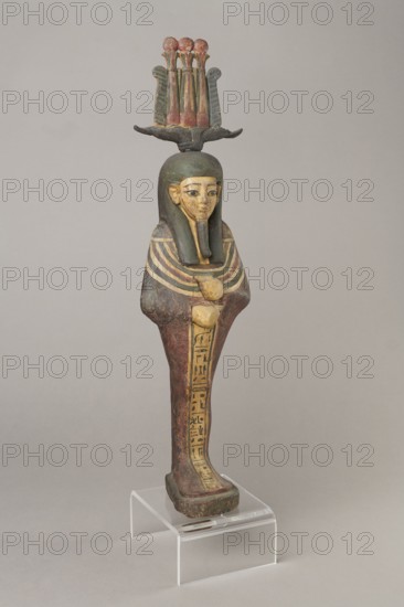 Osiris, Osiris mythology. Figurine in the form of a human mummy wearing a hemhem crown with ram's horns. On the chest is a usech necklace with falcon heads at the ends. Clenched hands are placed on the chest, one above the other. Below the right hand begins a column of text with the name and filiation. At the back, from the edge of the wig to the feet, a pillar with a column of hieroglyphic inscriptions — the beginning of a hymn to Osiris, the heir of Atum. The figurine is painted cherry red, the visible parts of the body are yellow, the wig is navy blue, and the necklace consists of white, red, and blue stripes. The background of the inscriptions is yellow. The figurine belongs to Isetemachbit, a musician of the god Amun-Re, daughter of the priest Mentuemhat; her mother was probably Takereret, known as Heres. Similar to type IV B according to Raven. 4th–3rd century BC; 30th Dynasty–early Ptolemaic period, Egypt. Sculpture; height 54.5 cm, width 12.5 cm, depth 9.5 cm., A painted wooden...