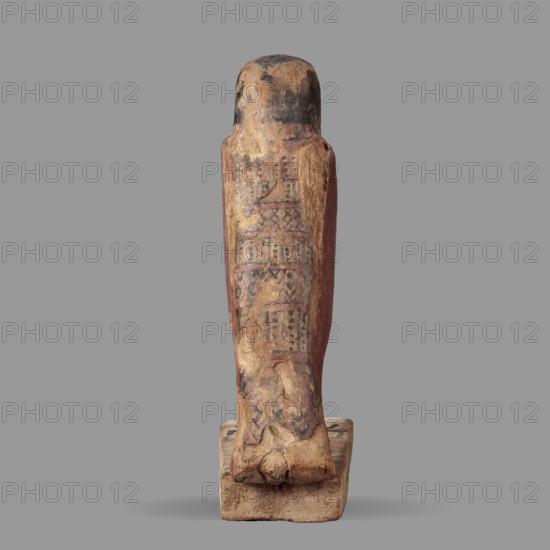 Figurine of the falcon Sokaris, guardian of the necropolis; Horus mythology. A falcon stands on a thick rectangular base, resting its tail on the back edge of the base. The bird's head is slightly raised. The beak is long and curved; the body is long, with wings slightly plastically defined in their upper part and the lower part of the wings merging with the tail. The head is black on the sides and back; the front of the head is yellow with a black diagonal check. The eye is marked with white and black paint. A white stripe encircles the neck. The wings are black and red. Bird legs with red and black lines. Late Period–Ptolemaic Period, 664–30 BC, Egypt. Sculpture; height 24.3 cm, width 20.5 cm., A weathered wooden figure standing on a rectangular base with a rounded head and an elongated body, showing worn painted decoration on its surface; the visible colors include beige, brown, black, and faded red, with areas of flaking and patchy wear revealing lighter wood beneath, and the base ...