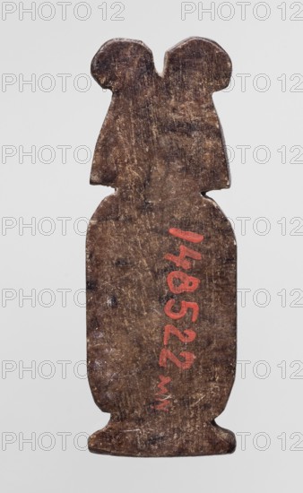 Amulet — cartouche with two ostrich feathers; amulet in the shape of a cartouche topped with a crown of ostrich feathers., Late Period, Egypt, 664–332 BC. Materials not specified. Height 4.3 cm; width 1.4 cm., An elongated, flat object with a worn, textured surface in shades of brown, shaped with a rounded lower body, a narrower midsection, and a top that splits into two rounded protrusions; a few lighter brown and beige scuff marks and darker brown spots appear across the surface, and there is a small area of red paint visible on the front; the background is a plain light gray.