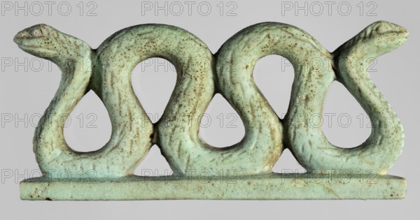 Amulet – two-headed snake;, Two-headed snake with vertical coils on a base, with delicately carved scales and snouts. Material: amulet. Function: protective amulet. Subject: snakes/animals. Style: Egyptian art. Date: 664–332 BC, Late Period, Egypt. Dimensions: height 3.3 cm, width 7 cm, depth 1.5 cm., A small sculptural object shaped like a horizontal row of three stylized looping serpents with raised heads at each end, rendered in a pale green color with a speckled brown patina and areas of slightly darker green; the piece sits on a flat rectangular base of the same pale green with brown speckling, and the background is a neutral light gray.