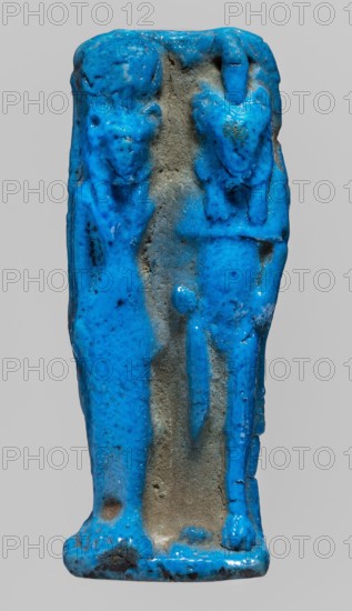 Amulet plaque with a relief representation of two deities: a lion-headed goddess in a long robe, with a sun disc and a uraeus on her head Sekhmet, and a naked lion-headed god with a uraeus on his head possibly Mahes. The god appears to have paws instead of arms and legs. Ptolemaic Period, 332–30 BC, Egypt. Amulet plaque. Height 6.7 cm; width 2.7 cm., A small sculpted object with a glossy bright blue surface covering most of its form, showing a vertical rectangular shape with worn and rough gray-brown areas where the blue glaze is missing, and a raised pair of simplified humanlike figures standing side by side with rounded heads, elongated torsos, and subtle limb suggestions; the surface shows irregularities, pits, and slight dark speckling within the blue, and the base is slightly flared with uneven edges and a mix of blue glaze and exposed darker material.