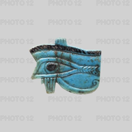 Amulet - Udjat Eye;, Udjat eyes; Ancient Egyptian; grave goods; amulet representing an eye with openwork eyeball, details marked schematically; Third Intermediate Period, ca. 945–656 BC 22nd–25th Dynasty, Egypt; amulet; height 3.4 cm, width 4.2 cm., A small carved object shaped like an eye with surrounding ornamental details, shown against a plain light gray background, featuring dominant turquoise blue with areas of darker teal and blackish brown discoloration and weathering, a central rounded dark spot within the eye area, a raised ridge along the top with darker mottling, a hooked projection at the left and a curved tail-like extension at the right, surface scratches and fine lines visible across the piece, and subtle variations of lighter blue and greenish tones on the lower edge.