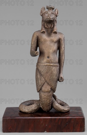 The god Anubis in the form of a jackal-headed deity, Anubis mythology. Figurine of Anubis in the form of a human-jackal-serpent in an upright posture, torso slightly tilted back, with a jackal head with a strongly elongated muzzle and a mane flowing down the back. He is dressed only in an Egyptian apron, below which the torso merges into the body of a snake with a striated abdomen and scaled skin, curled in a horizontal figure eight that supports the figurine. The left arm is held straight alongside the body with a clenched fist; the right is bent at the elbow, with the forearm extended forward. Three protrusions on the head between the ears. Late 1st–2nd century AD; Roman period, Egypt. Terracotta figurine, height 13.5 cm, width 7.1 cm, weight 0.936 kg with base., A small metallic statue of a humanoid figure with a textured brownish-bronze surface stands on a polished dark reddish-brown rectangular base; the figure has an animal-like head with prominent ears and a carved open mouth, a...