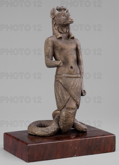 The god Anubis in the form of a jackal-headed deity, Anubis mythology. Figurine of Anubis in the form of a human-jackal-serpent in an upright posture, torso slightly tilted back, with a jackal head with a strongly elongated muzzle and a mane flowing down the back. Dressed only in an Egyptian apron, below which the torso merges into the body of a snake with a striated abdomen and scaled skin, curled in a horizontal figure-eight that supports the figurine. Left arm held straight alongside the body with a clenched fist; right arm bent at the elbow with the forearm extended forward. Three protrusions on the head between the ears. Late 1st–2nd century AD; Roman period, Egypt. Terracotta or unspecified material figurine; height 13.5 cm, width 7.1 cm, weight 0.936 kg with base., A bronze-colored statue of a standing anthropomorphic figure with an animal head and a mane, shown from head to base, mounted on a dark reddish-brown rectangular stone plinth; the figure has a bare torso, a wrapped lo...