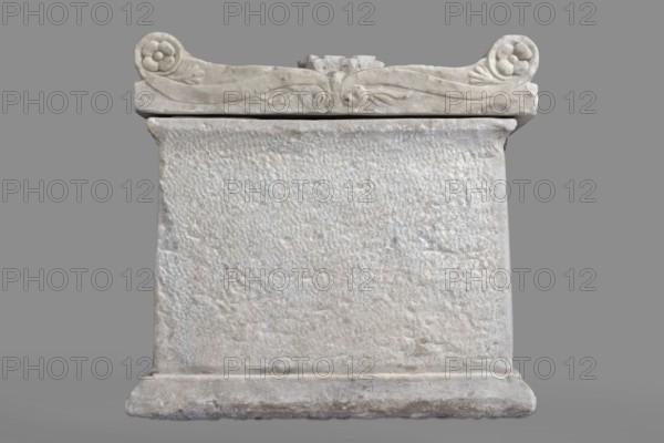 Urn with a depiction of swans, unknown Roman workshop. Sepulchral funerary architecture. Main plate: the urn's box is trapezoidal in shape, tapering towards the top. The urn is placed on a profiled base. Decoration of the front surface is sparse. The main part is occupied by a tabula ansata, the ears of which are decorated with palmettes. Below the inscription field are depictions of two swans in deep relief, facing each other with strongly arched necks; they appear to be taking flight, their outstretched wings touching the inscription frame. The upper part of the urn is crowned by a profiled cornice. On the inner upper edge, a rectangular protrusion used to secure the lid is visible. Side walls: no decoration. Metal pins visible under the cornice on both sides. Lid: original missing; currently fitted with a replacement lid. Dated to the 2nd half of the 1st century AD probably 3rd quarter of the 1st century AD or more broadly to the period 2nd half of the 1st – 1st half of the 2nd cent...