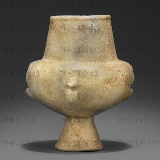 Stone vessel – kandila, Body in the shape of a flattened hemisphere with four evenly spaced, ribbed, vertical handles. The handles have round holes through their centers and slightly protrude into the surface of the body. Narrow, flattened shoulders. Neck clearly defined, wide, and conical. Spout in the form of a delicately defined roller running around the rim of the vessel. Interior hollowed out in the neck area with a shallow, semicircular recess protruding into the body; the remaining part of the belly is not hollowed out. 3200–2800 BC Early Cycladic I period, Grotta–Pelos culture, Cyclades. Vessel. Height 11.5 cm, width 9 cm, weight 0.734 kg., A rounded stone vessel on a flared pedestal, carved from a mottled light beige to creamy stone with areas of warmer tan and subtle grayish patches; the upper section tapers inward to a short neck and slightly rolled rim while the midsection bulges outward and shows a few shallow, irregular depressions; the surface appears slightly weathered ...