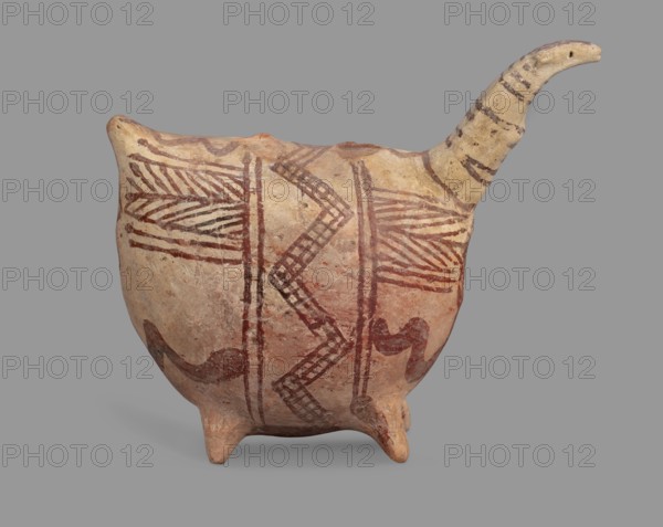Vessel in the shape of an animal, unknown Cypriot workshop. Fantastic animal-shaped vessel: long thin neck ending in a triangular, slightly flattened head; eyes marked with depressions; oblong flat ears. Geometric decoration covers the entire surface: at the widest point a band of zigzag filled with a checkered pattern; herringbone stripes radiate at right angles at front and back; beneath these are wavy stripes of paint; series of thin lines on the neck; a hole in the front under the neck. Cypriot pottery, 1900–1600 BC Late Bronze Age II, Cyprus. Vessel. Height 10.7 cm, width 12.5 cm, depth 6.8 cm., A rounded ceramic vessel with a short spout and three small rounded feet sits against a neutral gray background; the vessel shows a weathered beige and light tan base color with reddish-brown painted geometric patterns including zigzag and linear motifs and a few darker brown accent marks, and the spout is lighter beige with darker horizontal banding.