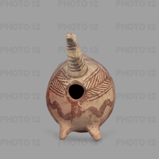 Vessel in the shape of a fantastic animal. The neck is long and thin, ending in a triangular, slightly flattened head. The eyes are marked with depressions; the ears are oblong and flat. Geometric decoration covers the entire surface. At its widest point, the body is surrounded by a band consisting of a zigzag band covered with a checkered pattern. From this band, herringbone stripes radiate at right angles at the front and back. Beneath these are wavy stripes of paint. A series of thin lines on the neck; a hole in the front under the neck. Terracotta vessel, Cyprus, 1900–1600 BC Late Bronze Age II. Height 10.7 cm; width 12.5 cm; depth 6.8 cm., A small rounded ceramic vessel with a short spout projecting from the top and three short pointed legs at the base, decorated with painted linear and wavy patterns; the surface shows earthy tones including beige, light tan, reddish-brown, and darker brown, with a central circular opening and striped markings on the spout and radiating hatch-like...