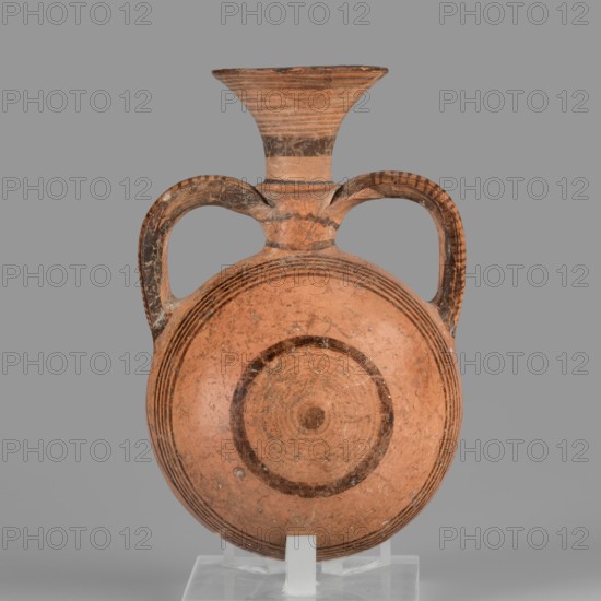 Bottle amphoriskos, Amphora with a round, slightly flattened flask-like belly. Brown-black decoration of concentric circles of varying thickness on the belly, horizontal lines on the rim, and a fine zigzag. Cypriot pottery, geometric motifs. 1050–750 BC Cypriot–Geometric Period. Cyprus. Vessel, height 10.4 cm, width 6.7 cm., A rounded terracotta vessel with a flared neck and two curved handles, shown against a plain gray background; the vessel is primarily warm orange-brown with darker brown painted bands and rings on the body, neck, and handles, and it displays surface wear and small spots of lighter discoloration; the piece rests on a translucent stand that is pale and slightly reflective.