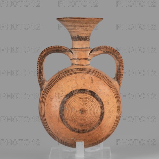 Bottle, Amphoriskos amphora with a round, slightly flattened flask-like belly. Brown-black decoration of concentric circles of varying thickness on the belly, horizontal lines on the rim, and a fine zigzag. Geometric motifs, circles iconography. Cypriot pottery, 1050–750 BC Cypriot-Geometric Period, Cyprus. Height 10.4 cm, width 6.7 cm., A round terracotta vessel with a flared neck and a pair of high curved handles, showing concentric painted bands and circular motifs in dark brown on an orange-buff body, with areas of wear and small chips, set against a plain gray background and supported by a clear stand; visible colors include orange-buff, dark brown, gray, and clear/transparent.