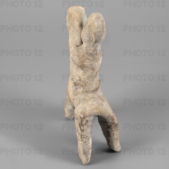 Figurine of a rider on a horse. The entire piece is schematic, the overall shape is highlighted, lacking any details. The horse is small, with a short torso, cylindrical, slightly tapering legs, and an unmarked tail. The neck is very long and vertical, the muzzle is large, the eyes are slightly convex, the ears are small, and the mane is short and trimmed. The rider sits upright, close to the horse's neck. The torso is short, the legs and arms are reflected. The head is large, with a clearly defined profile; the nose is particularly prominent, the eyes are unmarked, and at the back of the head is a vertically sloping, adjacent ridge that can be interpreted as a helmet plume. The helmet itself is not marked, only the overdeveloped top of the head suggests its presence. Date: 750–600 BC formerly dated 7th–6th century BC. Origin: Cyprus. Medium: figurine. Dimensions: height 14.9 cm, width 11.1 cm, depth 4 cm. Creator: unknown., A weathered, upright sculptural form with a rough, uneven sur...