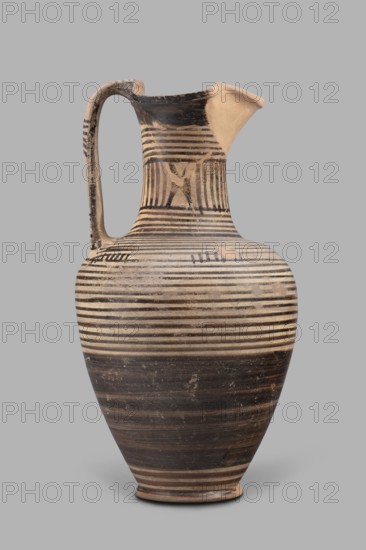 Oinochoe, Geometric oinochoe with a low foot, a gradually widening belly, distinct shoulders, a slender neck, and a tripartite rim characteristic of this vessel form. The vase runs from the shoulder to the rim. Halfway up the belly it is covered with black finish; the rest of the vessel is decorated with closely arranged parallel horizontal lines encircling the entire vessel. The central part of the neck is decorated with vertical stripes. Oinochoe was used for drawing and pouring wine Greek: oinos - wine and is a typical Greek vessel. Southern Italy Cumae workshop, end of the 8th century BC also dated end of 8th–beginning of 7th century BC; described as an Italian imitation of the Proto-Corinthian workshop. Vessel oinochoe; weight 0.476 kg; height 23.2 cm; diameter 12.2 cm., A tall ceramic jug with a rounded body, narrow neck, and spout, featuring a single curved handle; the surface shows a pattern of horizontal bands and stripes in black and beige, with a few areas of worn or lighter...