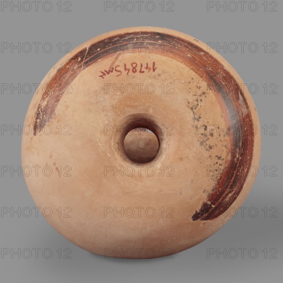 Askos, This ring-shaped askos incomplete, with visible restoration has a body tapering toward the top and a small neck terminating in a flared, profiled rim set diagonally to the upper edge. Dark banded decoration is painted on a light engobe: two wider bands on the upper part and bottom the lower band painted carelessly, fired unevenly and a delicate band with red varnish across the widest part. The varnish covers the rim, part of the neck, and the arched vice. Technology: purified clay with pyroxene admixtures; outer surface smooth, covered with engobe. Varnish matte, faded, in places burned red. Visible large losses, abrasions, scratches, and cracks. Clay color 5 YR 8/3 pink Engobe color 5 YR 7/6 reddish yellow Varnish color 5 YR 2.5/1 black Red color 2.5 YR 5/8 red Attributed to Kamila Nocon; 2nd half of the 6th century BC, Ionia. Vessel type: askos. Height 9.5 cm; width 9.1 cm; weight 0.16 kg; diameter 3.1 cm., A rounded terracotta object with a central circular hole, showing a sm...