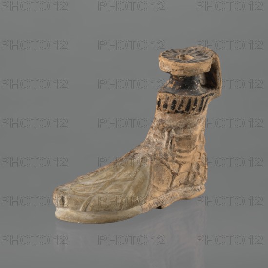 Foot-shaped aryballos, aryballos, antique vessel; Yellow-orange clay with mica; matte black engobe on the surface. Shaped as a foot wearing a sandal with a thick sole connected to braided leather straps. The foot ends above the ankle and merges into a narrow neck terminating in an outward-turned rim, decorated from above with radiating lines. A wide, ribbon-like handle is attached vertically to the spout, on which there is an image of a rooster surrounded by dots. Preservation condition: the front part of the foot is filled with plaster. End of the 6th–beginning of the 5th century BC; unknown Ionian workshop; Ionia Turkey/Greece., An object shaped like a foot with an attached ankle and short calf, rendered in earthy tan and beige tones with areas of darker brown and black, shows a textured surface with carved lines suggesting toes and instep on the forepart and layered, irregular surface on the ankle and heel; the top of the calf has a circular, dish-like element with radiating grooves...