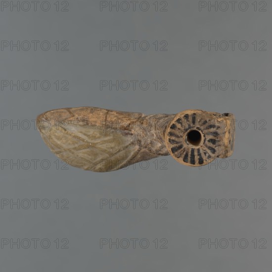 Foot-shaped aryballos, unknown Ionian workshop, aryballos, antique vessel, yellow-orange clay with mica, matte black engobe on the surface. Aryballos in the shape of a foot shod in a sandal with a thick sole connected to braided leather straps. The foot ends above the ankle and merges into a narrow neck terminating in an outward-turned rim, decorated from above with radiating lines. A wide, ribbon-like handle is attached vertically to the spout, on which there is an image of a rooster surrounded by dots. Preservation condition: the front part of the foot is filled with plaster. End of the 6th–beginning of the 5th century BC, Ionia Turkey/Greece, vessel., A weathered object resembling a small carved figure with an elongated wing-like projection on one side and a rounded hollow on the other, showing a surface of earthy tan and brown tones with patches of pale green on the wing area and darker brown to black radial markings around the circular opening, set against a uniform gray backgroun...