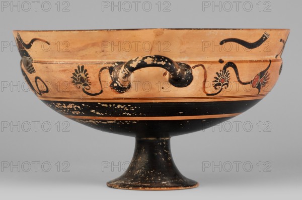 Kylix with a depiction of a mermaid and sphinxes, Griffin-Bird Painter; fantasy creatures iconography: sphinxes, sirens; Greek pottery, Attic kylix, ca. 570–550 BC previous dating ca. 545 BC; vessel; weight 0.314 kg., A shallow, wide bowl on a flared pedestal with a curved handle on each side, shown against a neutral gray background; the upper exterior of the bowl is a warm terracotta color with black painted decorative motifs including sinuous lines and stylized floral shapes, with small areas of red within some motifs, while the lower exterior and pedestal are painted black with areas of wear revealing the underlying terracotta, and the handles show chipped black paint exposing lighter areas.