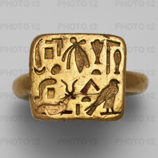 Gold ring of the high priest of the goddess Bastet, Hapimen ca. 664–525 BC. Goldsmithery; gold ring with a rectangular plaque on a circular thick-cylinder hoop. Upper surface of the plaque covered with two rows of hieroglyphic inscription in concave relief. Date: 664–525 BC, Late Period, 26th Dynasty. Possible origin: Leontopolis, possible findspot: Tell el-Moqdam . Subject: Hapimen, Bastet. Dimensions: total length 2.6 cm, width 2.6 cm; eyelet height 1.6 cm, width 1.8 cm; ring thickness 0.4 cm., A gold ring with a square bezel engraved with a group of carved symbols and small pictorial shapes, showing a bird figure, an insect-like motif, a reclining animal shape, and various geometric and curved forms; the ring and bezel are metallic gold in color with small areas of darker brownish or reddish insets within some carved lines, set against a neutral light gray background.