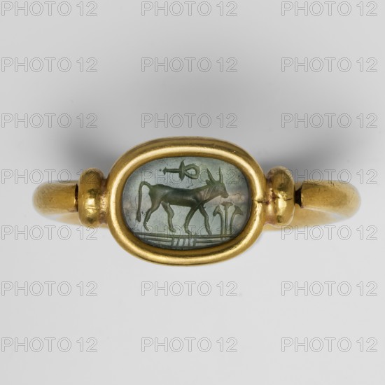 Ring with a scarab and a cryptogram of Amun. Amun mythology, ankh iconography, plant decorations; jewelry, Egyptian art, goldsmithery. The underside of the base is engraved: a bull visible in right profile with the ankh sign above it; in front of the bull on the right side is a tuft of vegetation. At the bottom, a double horizontal line interrupted by three lines — probably a cryptogram of the name Amun. c. 1550–c. 1295 BC; New Kingdom, 18th Dynasty, Egypt. Scarab amulet ring., A gold ring with a smooth, rounded band and an oval bezel containing a translucent greenish-blue gemstone engraved with a small animal figure and simple linear designs; the ring is shown against a neutral light gray background, and the visible colors include gold and greenish-blue.