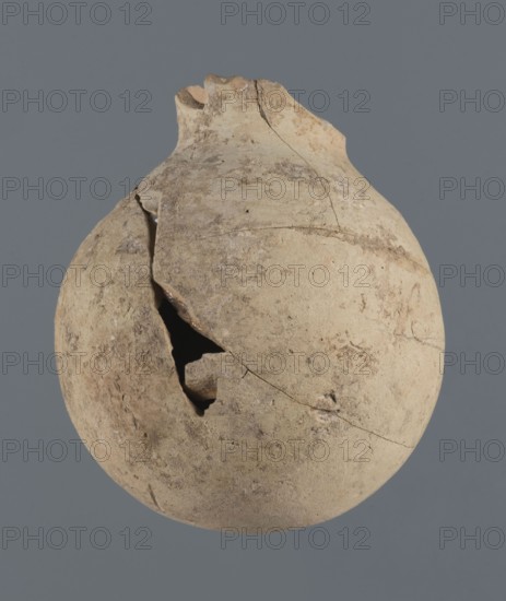 Globular vessel, unknown Northern Mesopotamian workshop Khaburu Basin, vice-free vessel from excavations of the Centre of Mediterranean Archaeology, Early Jazira III period ca. 2600–ca. 2350 BC. Vessel for oils and ointments, clay; Early Dynastic III period ca. 2600–ca. 2350 BC. Al-Jazira Syria/Iraq, Mesopotamia. Globular vessel with a spherical belly that at 3/4 height merges into short, sloping shoulders with a narrow, slightly flared neck; part of the neck and spout is missing. c. 2600–c. 2350 BC; Northern Mesopotamia Khabur basin, Tell Jassa el Gharbi north-eastern Syria. Vessel; height 13 cm, width 10.9 cm., A round, weathered clay vessel with a rough, cracked surface sits against a plain gray background; the vessel is primarily beige with patches of light tan and pale brown, showing mottled discoloration and darker brown speckles; the top is broken and irregular with a jagged rim, and a large triangular hole and several fractures run down one side revealing a dark interior; the s...