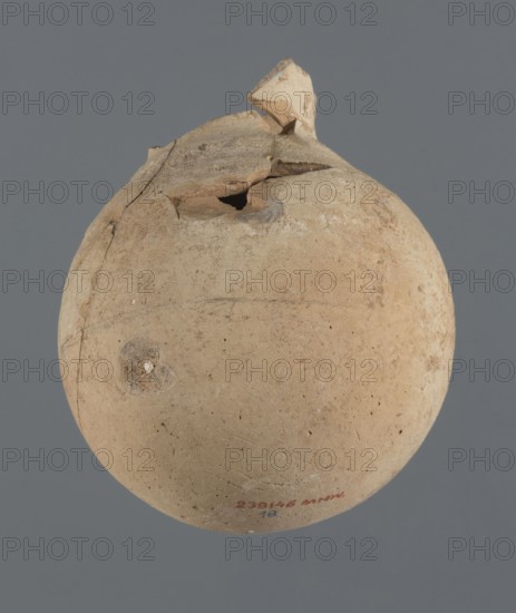 Globular vessel, unknown Northern Mesopotamian workshop Khaburu Basin, Early Jazira III period ca. 2600–ca. 2350 BC. Vessel for oils and ointments, clay; globular vessel with a spherical belly that at 3/4 of the height merges into short, sloping shoulders with a narrow, slightly flared neck. Part of the neck and spout is missing. Early Dynastic III period ca. 2600–ca. 2350 BC. Al-Jazira Syria/Iraq, Mesopotamia; Tell Jassa el Gharbi Khabur basin, north-eastern Syria. Height 13 cm, width 10.9 cm., A rounded pottery object with a rough, worn surface in shades of beige and light brown sits against a plain gray background; the top area is broken with jagged fragments and an irregular opening, and there are a few surface imperfections and spots of darker brown and pale discoloration across the body.