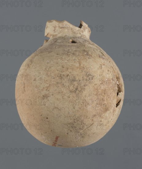 Globular vessel, unknown Northern Mesopotamian workshop Khaburu Basin, vice-free vessel, Early Jazira III period ca. 2600–ca. 2350 BC, vessel for oils and ointments, clay, Early Dynastic III period ca. 2600–ca. 2350 BC, Al-Jazira Syria/Iraq, Mesopotamia, globular vessel with a spherical belly that at 3/4 height merges into short sloping shoulders with a narrow, slightly flared neck; part of the neck and spout missing. Origin: Northern Mesopotamia Khabur basin, Tell Jassa el Gharbi Tell Jassa el-Gharbi, north-eastern Syria. Vessel; height 13 cm, width 10.9 cm., A rounded, weathered clay object with an irregular broken top sits against a plain gray background; the surface shows a mottled, rough texture with areas of lighter beige, tan, and darker brown discoloration, and a few small chips and cracks along the sides and near the top.