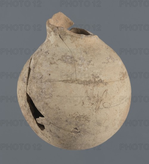 Globular vessel, unknown Northern Mesopotamian workshop Khaburu Basin, vice-free vessel from excavations of the Centre of Mediterranean Archaeology, Early Jazira III period ca. 2600–ca. 2350 BC, vessel for oils and ointments, clay, Early Dynastic III period ca. 2600–ca. 2350 BC, Al-Jazira Syria/Iraq, Mesopotamia, globular vessel with spherical belly that at 3/4 height merges into short, sloping shoulders with a narrow, slightly flared neck; part of the neck and spout missing; c. 2600–c. 2350 BC; Northern Mesopotamia Khabur basin, Tell Jassa el Gharbi north-eastern Syria; vessel; height 13 cm, width 10.9 cm., A weathered rounded clay vessel with an irregular broken rim and several cracks, showing rough, uneven surface texture and chips; the vessel appears in shades of beige, tan, light brown, and off-white against a solid medium gray background.