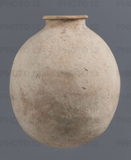 Bottle, unknown northern Mesopotamian workshop, Early Jazira III period ca. 2600–ca. 2350 BC / Early Dynastic III period ca. 2600–ca. 2350 BC. Clay vessel bottle with a bulging, regularly ovoid belly, rounded bottom, low narrow neck and thickened, slightly inclined spout. On the belly, at one-quarter height, a shallowly engraved potter’s mark in the form of a single sinusoidal-zigzag vertical line. Pottery from Tell Jassa el Gharbi north-eastern Syria, Northern Mesopotamia Khabur Basin. Height 34.6 cm; width 29.4 cm., A large rounded clay vessel with a narrow flared rim, shown against a flat gray background; the vessel's surface is matte and textured with an overall pale beige and light tan coloration, with areas of muted brown and faint greenish-gray patches, small scratches and surface irregularities visible across its body.