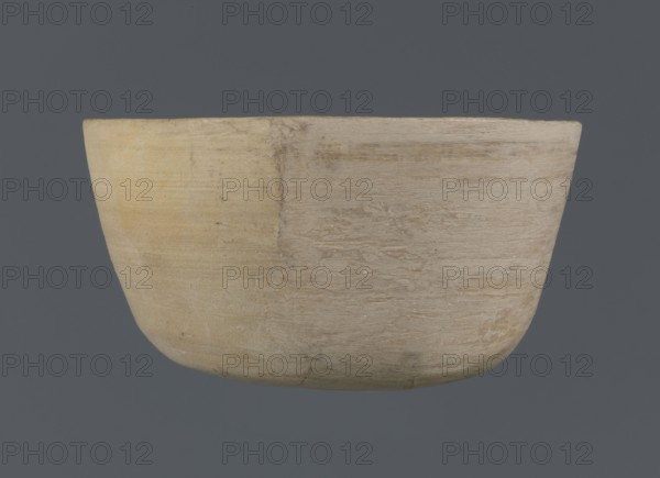 Bowl, unknown northern Mesopotamian workshop; Early Jazira III period ca. 2600–ca. 2350 BC / Early Dynastic III period ca. 2600–ca. 2350 BC; clay bowl, table vessel; Al-Jazira Syria/Iraq, Mesopotamia, Northern Mesopotamia Khabur basin; from Tell Jassa el Gharbi north-eastern Syria; bowl with a flat oval bottom, straight slightly tilted walls rising in a short arc, terminating in a straight, not distinct rim; ca. 2600–ca. 2350 BC; vessel; height 7 cm, width 12.2 cm., A simple rounded container with a smooth curved form occupying the center of the image, showing a worn surface texture with visible grain and subtle scratches; its colors include pale beige, light tan, creamy off-white, and hints of muted yellow against a solid dark gray background.