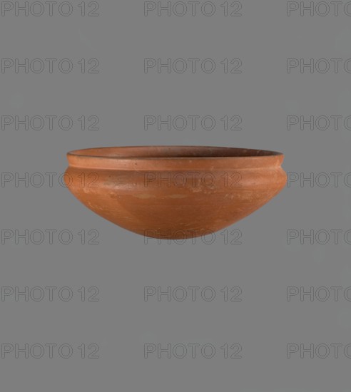 Medum-type bowl, Clay vessel, Medum-type bowl with characteristic carination under the rim. Rounded bottom, straight slightly flaring rim, narrow sloping shoulders; rim diameter smaller than shoulder diameter. Made of Nile clay, light red, well fired. Surface leveled, coated with engobe and polished. Outside of the lower body bears a hieroglyphic sign in the shape of a bird, probably the letter m. Vessel color red. Complete and very well preserved. Height 8.9 cm; rim diameter 20.9 cm; shoulder diameter 21.5 cm. Old Kingdom, ca. 2686–2181 BC., A simple terracotta bowl floating against a flat gray background, showing a rounded exterior with a slightly flared rim and a smooth, worn surface in shades of reddish-brown and muted orange with lighter patches and subtle darker spots.