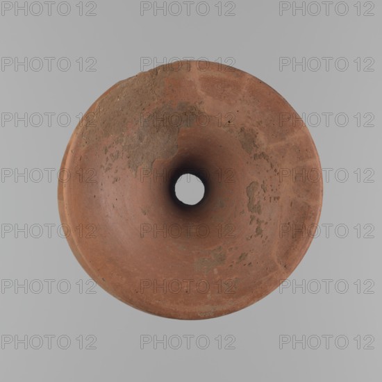 Vessel base, Funnel-shaped vessel base, narrowest at about 2/3 of the height. Both rims are oval in cross-section, slightly upturned. The upper rim has a slightly wavy line. The vessel is made of Nile clay. The outer surface and the surface of the upper rim are smoothed, covered with a layer of engobe and polished. Only the remaining inner surface is smoothed. Vessel color - red. Vessel glued together from several fragments. Gaps filled with plaster. The surface of the vessel is eroded in places. Comparative material: Reisner, A history of Giza necropolis, vol. I, fig. 282, C,4240, ca. 2686–2181 BC; Old Kingdom, Edfu, vessel, height 23.9 cm, diameter 16.9 cm rim, diameter 19.6 cm bottom, A top-down view of a round, funnel-shaped object with a central circular hole, showing a surface of reddish-brown clay with patches of darker brown and some lighter tan areas, set against a smooth light gray background.