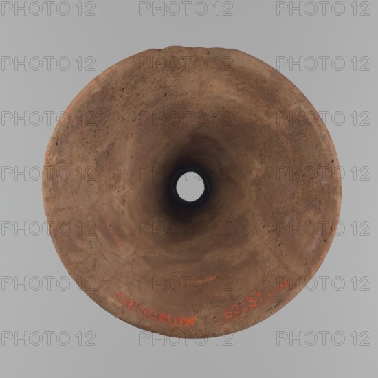 Vessel base. Funnel-shaped vessel base, narrowest at about 2/3 of the height. Both rims are oval in cross-section, slightly upturned; the upper rim has a slightly wavy line. Made of Nile clay. Outer surface and surface of the upper rim smoothed, covered with a layer of engobe and polished; remaining inner surface smoothed. Vessel color: red. Reassembled from several fragments; gaps filled with plaster. Surface eroded in places. Comparative reference: similar form illustrated by Reisner fig. 282, C,4240, dated to the Old Kingdom, ca. 2686–2181 BC. Dimensions: height 23.9 cm; rim diameter 16.9 cm; bottom diameter 19.6 cm. Origin: Edfu. Creator: unknown., A top-down view of a round, hollow object with an inward-sloping funnel shape, showing a rough, weathered surface in shades of brown and tan with variations of darker brown around the central opening; the background is a flat light gray.