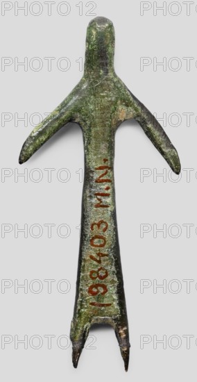 Votive figurine of a woman, votive offering, bronze female figurine, 1st half of the 6th century BC, Etruria; height 6.1 cm, width 2.9 cm, depth 0.5 cm., A weathered metal object shaped like a stylized human figure with an elongated body and a rounded head, showing a greenish patina with areas of darker brown and lighter green; it has a pair of outstretched arm-like projections and a split lower end forming two pointed prongs, with traces of reddish-brown markings along the central shaft.