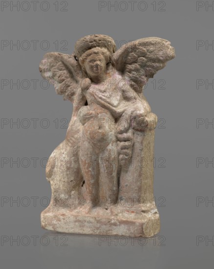Terracotta figurine of Eros with a goose. Terracotta; figurine of a standing Eros. The figure, positioned frontally, slightly leaning back and facing left, stands on a low rectangular base. On the left he leans against a small column; on the right he holds a goose by the neck. The left hand, clasped at the elbow, rests on the top of the column, holding a short cloak halfway up. The cloak, fastened with a fibula over the right shoulder, covers the chest and forms folds and flows along the small column. Hair arranged in curls, covered in the upper part by a high diadem. Outstretched wings with straight, defined feathers, slightly tilted back. Scratches faded, traces of polychromy. 2nd half of the 1st century BC, Asia Minor. Figurine; height 14 cm, width 10.2 cm, depth 3.4 cm, weight 0.18 kg., A small weathered sculpture of a seated winged figure rendered in rough textured stone sits on a rectangular base; the figure has a round head with a simple hair or headband form, a softly modeled f...