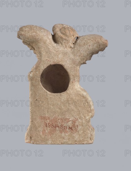 Terracotta figurine of Eros with a goose. Terracotta; figurine of a standing Eros molded from a mold. The figure, positioned frontally, slightly leaning back and facing left, stands on a low rectangular base. On the left he leans against a small column; on the right he holds a goose by the neck. The left hand, clasped at the elbow, rests on the top of the column and holds a short cloak halfway up. The cloak, fastened with a fibula over the right shoulder, covers the chest and forms folds and flows along the small column. Hair arranged in curls, covered in the upper part by a high diadem. Outstretched wings with straight, defined feathers slightly tilted back. Scratches faded, traces of polychromy. 2nd half of the 1st century BC, Asia Minor. Figurine; height 14 cm, width 10.2 cm, depth 3.4 cm, weight 0.18 kg., A weathered beige-brown sculpted object with a rough, textured surface and a rounded hollow near its upper center; the top has a form suggesting two wing-like protrusions and a ce...