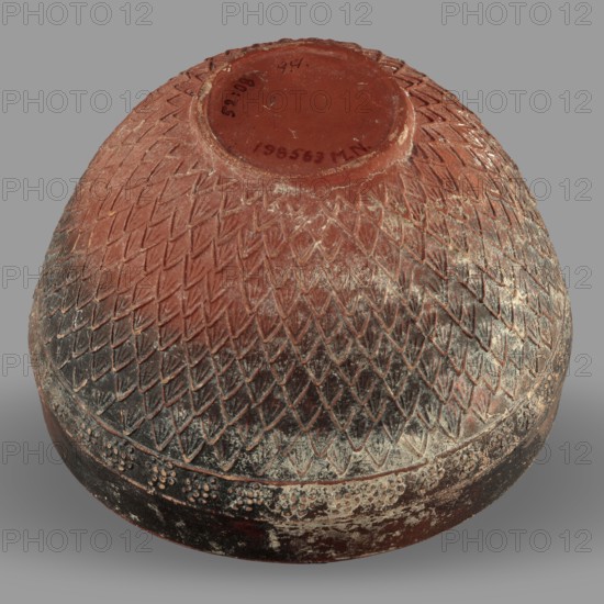 Megarian bowl, unknown Ionian workshop, Classified Gallic Scenography, end of 2nd–beginning of 1st century BC, Ionia Turkey/Greece; vessel; height 8.5 cm, width 13.1 cm, weight 0.178 kg., A rounded vessel shown upside down with a textured surface of overlapping V-shaped impressions forming a scale-like pattern, a band of small raised dots near the base, and a recessed circular foot; visible colors include reddish-brown, dark brown to nearly black, pale white residues, and shades of gray in the background.