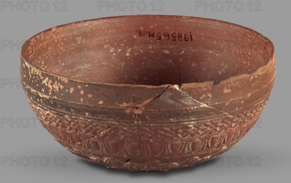 Megarian bowl, Monogramist's Workshop, 2nd half of the 2nd century BC, Ephesus, Ionia; vessel; weight 0.134 kg, A broken shallow bowl with a rounded shape and a textured lower band, showing a few cracks and missing rim fragments; the surface displays several patches of flaking and small speckled areas. The bowl is primarily reddish-brown with darker brown bands and some lighter beige or tan spots where the surface has worn away. The background is a flat gray.