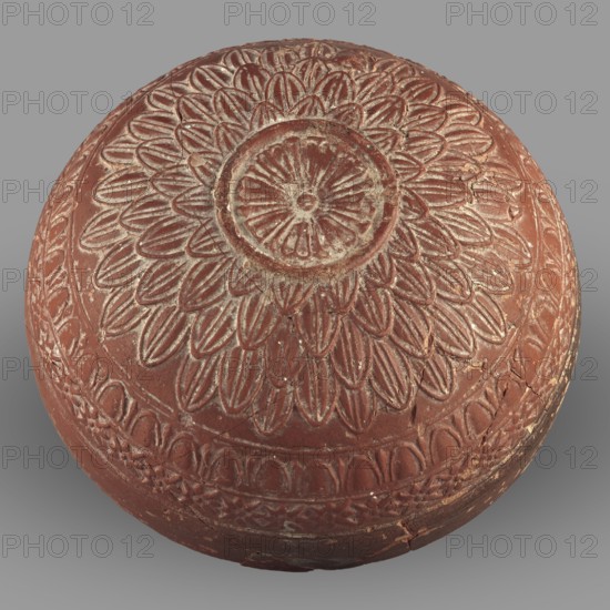 Megarian bowl, Monogramist's Workshop, 2nd half of the 2nd century BC, Ephesus, Ionia; vessel, weight 0.134 kg, A round carved object with a dome shape featuring a central circular motif surrounded by a radiating petal pattern, the carvings showing worn edges and surface abrasions; the piece displays a reddish-brown base color with lighter beige highlights where the carved lines and wear reveal a paler tone, set against a neutral gray background.