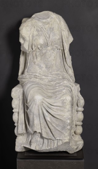 Statue of the goddess Cybele on a throne, Cybele myth., statues of deities, Roman sculpture, 1st century BC–1st century AD, Asia Minor, sculpture; height 84 cm, width 43 cm, depth 39 cm, weight 181 kg, A seated marble statue fragment showing the torso and lower body of a draped figure on a sculpted chair, with flowing carved folds and layered fabric details, missing the head and parts of the arms; the stone appears weathered with a pale off-white surface and subtle gray and beige mottling, set against a dark gray background with a dark pedestal beneath.