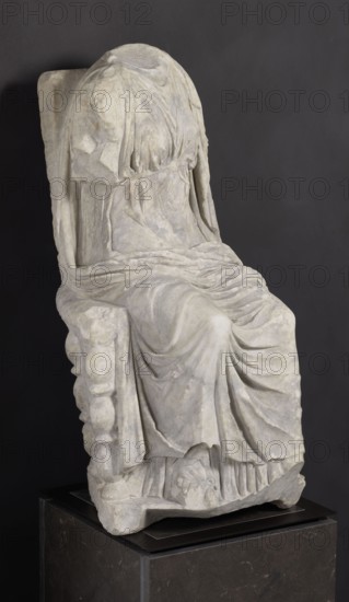 Statue of the goddess Cybele on a throne; creator, Cybele myth., statues of deities; Roman sculpture, 1st century BC–1st century AD; Asia Minor possibly; sculpture; height 84 cm, width 43 cm, depth 39 cm, weight 181 kg., A draped seated stone figure on a pedestal, shown against a dark gray background, with the drapery forming flowing folds and pleats over the torso, arms, and legs; the head is covered and lacks facial details, and the figure’s garments show textured surfaces and soft curves; the seat has a sculpted side with rounded protrusions and the base rests on a dark rectangular pedestal. Colors visible include shades of light gray and off-white on the sculpture, dark gray on the background, and darker gray and black tones on the pedestal.