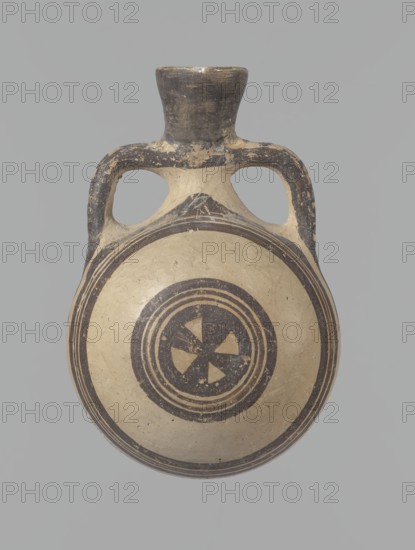 Canteen, Cyprus. Canteen decorated with concentric circles. Vessel with a spherical, slightly flattened body width on one side 8.5 cm, on the other 7.3 cm and two vertical, cylindrical vises and a narrow neck. Slightly flaring spout reconstructed. Pinkish clay. Creamy engobe, black-brown decoration. On the handles, horizontal lines framed on the sides by thick lines, which are connected at the neck at the attachment point, while below the vises they intersect below the handles. The two flattened sides of the body are decorated identically. Two sets of concentric circles, composed of four lines each: two narrow lines framed on both sides by wider lines. The outer line of the outer band overlaps the neck of the vessel and slightly extends over the vice mounts, widening in these places. The center of the inner band is filled with a Maltese cross motif. Good condition: reconstructed spout and upper half of the neck. Limescale deposits have been removed from the surface of the vessel. Numer...