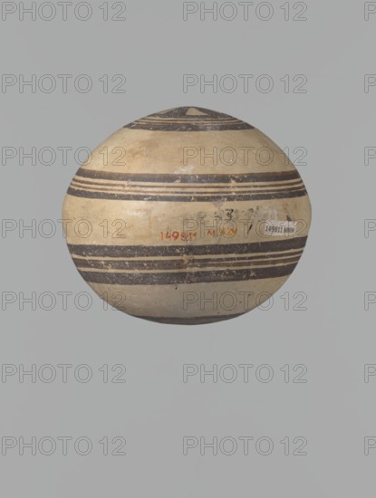 Canteen, Cyprus, Cypriot ceramics, White Painted I . Canteen decorated with concentric circles. Vessel with a spherical, slightly flattened body width on one side 8.5 cm, on the other 7.3 cm and two vertical, cylindrical vises and a narrow neck. Slightly flaring spout reconstructed. Pinkish clay. Creamy engobe, black-brown decoration. On the handles, horizontal lines framed on the sides by thick lines, which are connected at the neck at the attachment point, while below the vises they intersect below the handles. The two flattened sides of the body are decorated identically. Two sets of concentric circles, composed of four lines each: two narrow lines framed on both sides by wider lines. The outer line of the outer band overlaps the neck of the vessel and slightly extends over the vice mounts, widening in these places. The center of the inner band is filled with a Maltese cross motif. Good condition: reconstructed spout and upper half of the neck. Limescale deposits have been removed f...