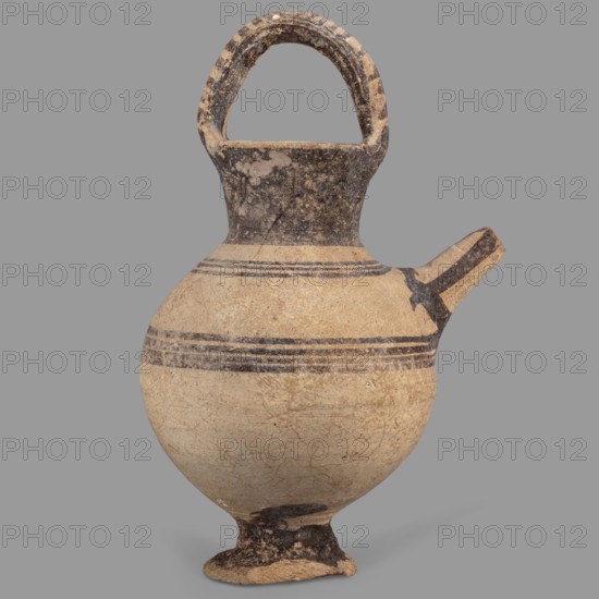 Jug on a ring-shaped foot, from which a low, wide stem extends, transitioning into a belly. The upper part of the spherical body has a narrow spout. The wide, flaring neck terminates in a simple spout, from both sides of which a vice, shaped like a flattened cylinder, extends above the vessel. Decoration in brown varnish: concentric circles surrounding the vessel four below and three above the spout. The foot and stem are varnished on the top, and the neck and side edges of the vice are varnished on the outside. The upper part of the vice is decorated with a row of transverse stripes. A strip of varnish encircles the spout at the base, and three stripes decorate the spout on the sides and top., 1050–950 BC; Cyprus, Geometric period I Cyprus-Geometric District IA. Vessel. Height 12.8 cm; width 6.5 cm., The image shows an ancient-looking rounded ceramic vessel with a narrow neck and an arched handle attached to the top, a short angled spout on one side, and a small footed base; the surfa...