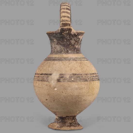 Jug, Jug on a ring-shaped foot, from which a low, wide stem extends, transitioning into a belly. The upper part of the spherical body has a narrow spout. The wide, flaring neck terminates in a simple spout, from both sides of which a vice, shaped like a flattened cylinder, extends above the vessel. Decoration in brown varnish: concentric circles around the vessel four below and three above the spout. The foot and stem are varnished on the top; the neck and side edges of the vice are varnished on the outside. The upper part of the vice is decorated with a row of transverse stripes. A strip of varnish encircles the spout at the base, and three stripes decorate the spout on the sides and top. Dated 1050–950 BC; Cyprus, Geometric period I Cyprus-Geometric District IA. Vessel; height 12.8 cm, width 6.5 cm., A rounded ceramic vessel with a narrow flared neck, a single arched handle extending from the neck to the rim, and a small flared foot. The surface shows a worn, matte texture with areas...