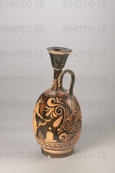 Red-figure aryballus lekythos with a depiction of Eros and a woman, Darius Painter 340–320 BC, Apulia, vessel lekythos/aryballus, height 23.3 cm, width 10.7 cm., An upright ceramic vessel with a narrow neck, a flared rim, and a single curved handle rising from the shoulder; the body displays sweeping ornamental spirals and leaf-like motifs in a terracotta-orange against a black background, with areas of worn black showing lighter ceramic beneath; the rim and neck are predominantly black with chipped edges revealing a tan color, and the base shows concentric bands in tan and black; the overall scene includes a few areas of surface wear and a muted gray background.
