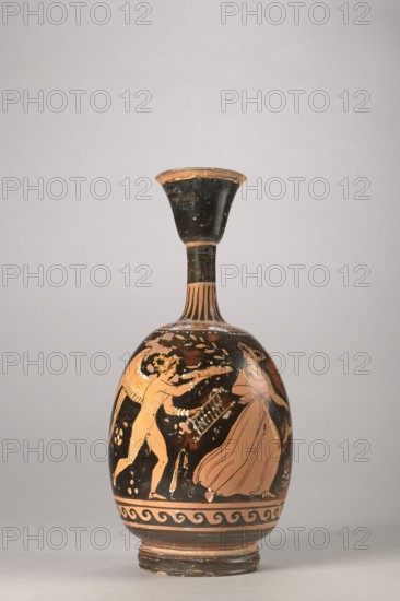 Red-figure aryballus lekythos with a depiction of Eros and a woman, Darius Painter active 340–320 BC, Apulia; vessel lekythos, aryballus lekythos, height 23.3 cm, width 10.7 cm, 340–320 BC., The image shows a ceramic vessel with a long narrow neck and a flared rim, set against a plain light gray background. The vessel displays a black surface with reddish-orange figures and decorative elements. On the rounded body there is a scene with a winged nude figure facing a robed figure, both rendered in reddish-orange on the black ground. The neck and rim are mostly black with some worn reddish-orange edges, and the shoulder has vertical ribbed decoration in reddish-orange. The lower body has a patterned band in black and reddish-orange above a stepped rounded base that shows areas of black and reddish-orange wear.