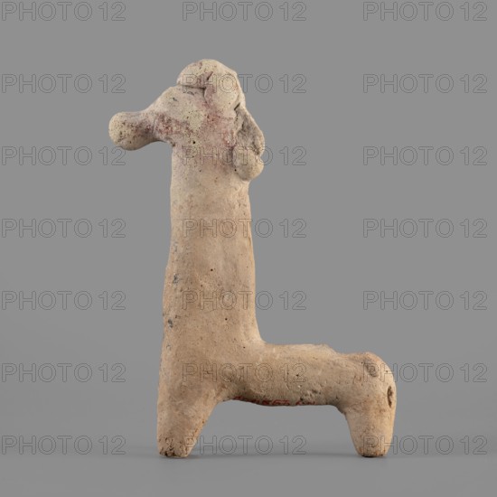 Horse figurine, unknown Cypriot workshop. Schematic horse figurine. Plastically modeled muzzle, strongly rounded at the tip. Eyes marked with convexities. Mane attached. Neck strongly elongated in relation to the rest of the body, flattened at the rear edge, imitating a mane. Body narrow in relation to the neck, cylindrical. Front legs spread out to the sides, also cylindrical. Hind legs designed as a single unit in the form of a cylinder. Traces of polychrome visible on the surface: muzzle and mane reddish-brown, eyes highlighted in black. Traces of black paint also visible on the neck and chest of the animal. 750–600 BC Cypro-Archaic period II, Cyprus. Terracotta figurine, height 10.8 cm, width 7.8 cm., A clay figurine shaped like an abstract animal or creature stands against a gray background; its surface is rough and textured with visible pitting and small holes, and its overall color is a pale beige with patches of light brown and faint reddish areas, especially near the head and ...