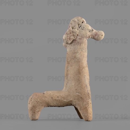Horse figurine, unknown Cypriot workshop. Schematic horse figurine. Plastically modeled muzzle, strongly rounded at the tip. Eyes marked with convexities. Mane attached. Neck strongly elongated in relation to the rest of the body, flattened at the rear edge, imitating a mane. Body narrow in relation to the neck, cylindrical. Front legs spread out to the sides, also cylindrical. Hind legs designed as a single unit in the form of a cylinder. Traces of polychrome visible on the surface: muzzle and mane reddish-brown, eyes highlighted in black. Traces of black paint also visible on the neck and chest of the animal. 750–600 BC previously dated 6th century BC; Cypro-Archaic II, Cyprus, terracotta figurine, height 10.8 cm, width 7.8 cm., A weathered clay sculpture of an animal-like form stands against a plain gray background, showing a tall vertical body with a horizontal limb at the base creating an L-shaped silhouette; the surface is rough and pitted with irregular texture and small holes, ...